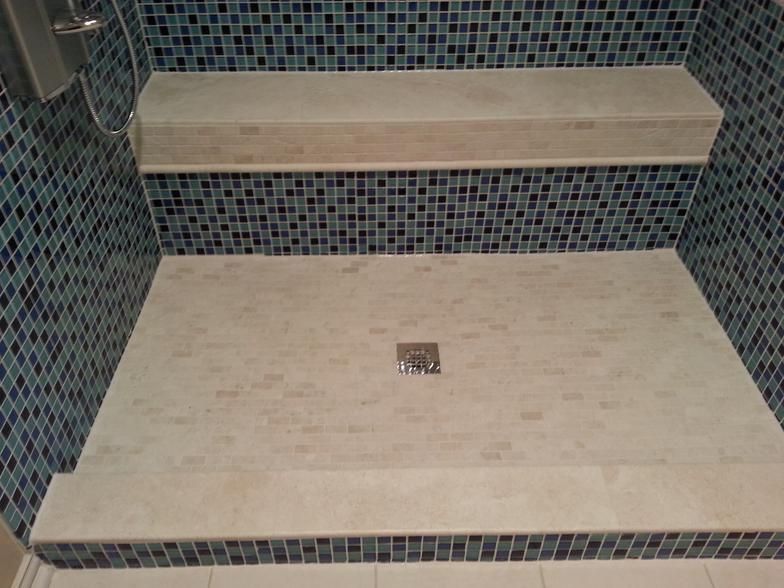 Shower stall with light-colored tile base, blue mosaic tile walls, and a shelf.