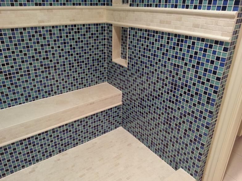 Mosaic-tiled shower with a built-in bench and shelf. Blue, green, and white tiles with light beige trim.