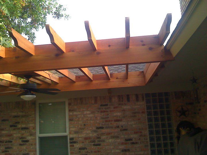 Wooden pergola attached to a brick building. Overhead view, includes a ceiling fan and a window.