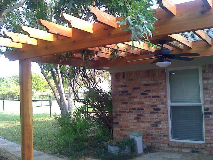Wooden pergola attached to brick wall, with a ceiling fan.