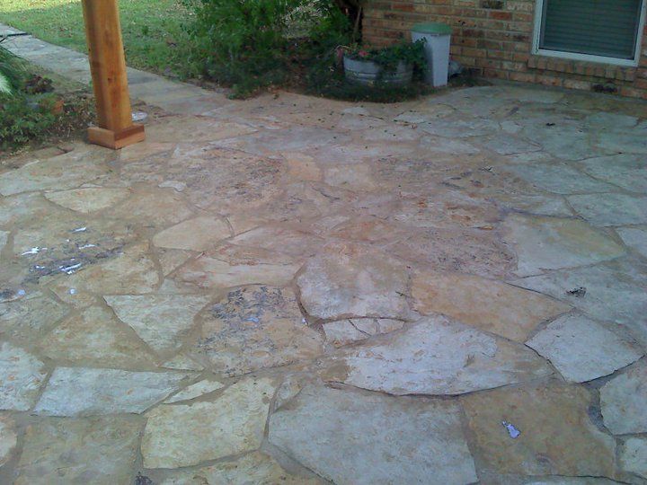 Stone patio with irregularly shaped flagstones, next to a brick building and a wooden post under a porch.
