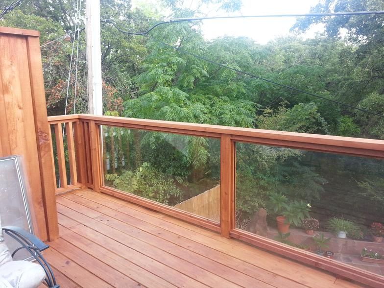Wooden deck with glass railing overlooking lush green trees.
