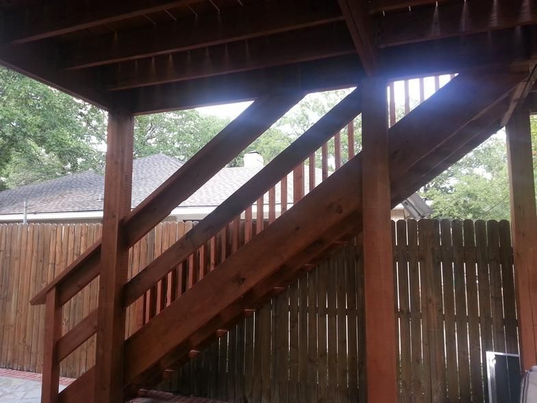 Wooden outdoor staircase leading up, stained brown, with railing and support beams.