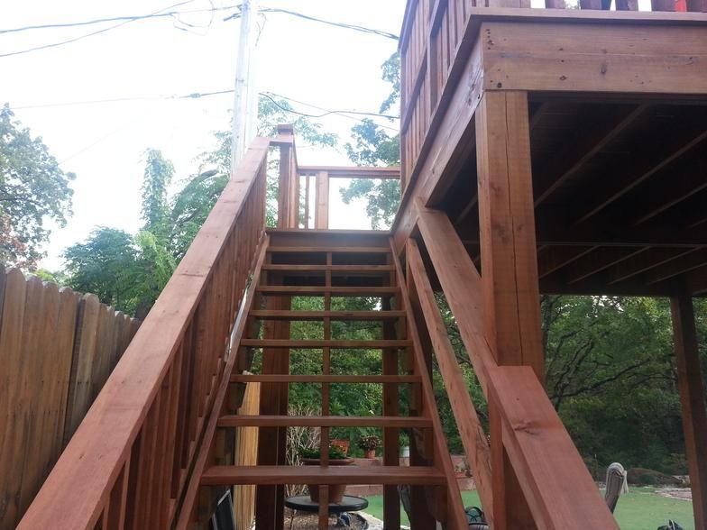 Wooden outdoor staircase leading up to a playhouse. Brown stain, railing, overcast day.
