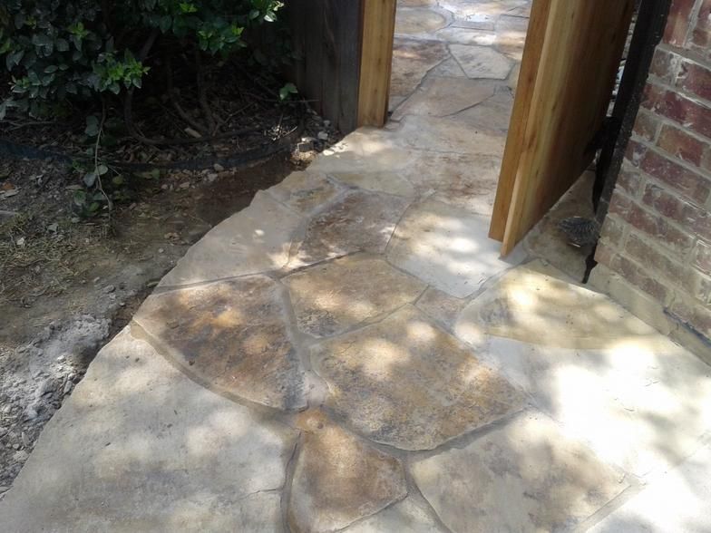 Flagstone path leading to a wooden gate and brick wall, shaded by trees.