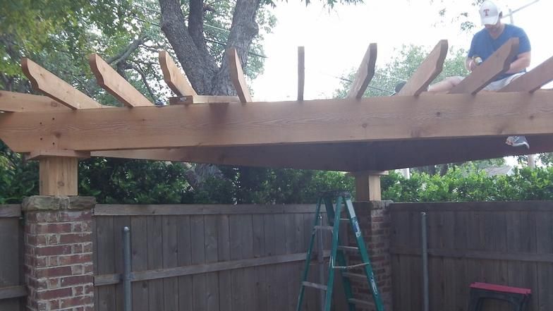 Man building a wooden pergola over a brick and wood fence.