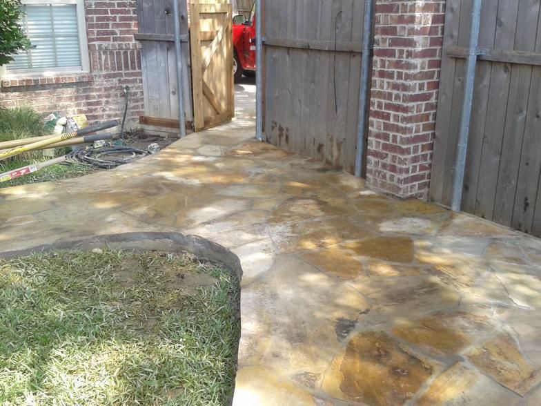 Flagstone pathway leading to a wooden gate and brick column, with a patch of grass in the foreground.