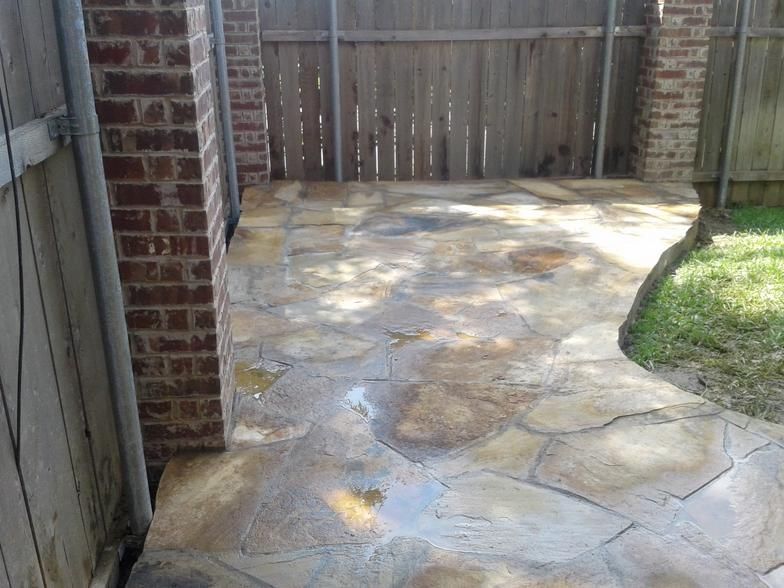 Stone patio with brick columns and wooden fence in a backyard setting.