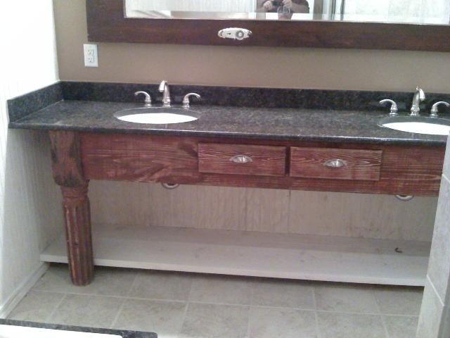 Bathroom vanity with two sinks, dark countertop, wooden cabinet, and decorative legs.