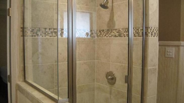 Shower stall with glass doors, beige tiles, and mosaic accent.