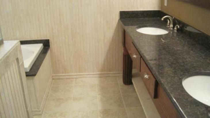 Bathroom with a dark granite countertop, two sinks, and a bathtub. Beige tile and wallpaper.