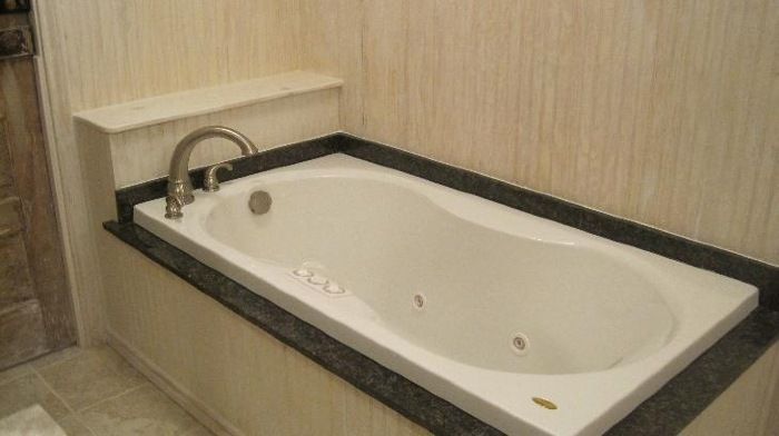 Built-in white bathtub with dark gray trim. Silver faucet and a small shelf are against light-colored wall.