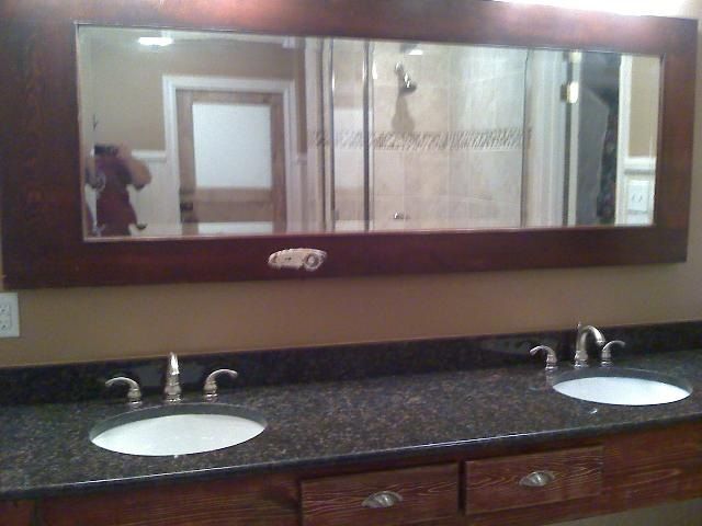 Bathroom with a large rectangular mirror above a double sink vanity with dark granite countertop.