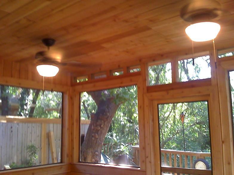 Sunroom interior with wooden ceiling, windows, and ceiling fans, with a view of a tree.