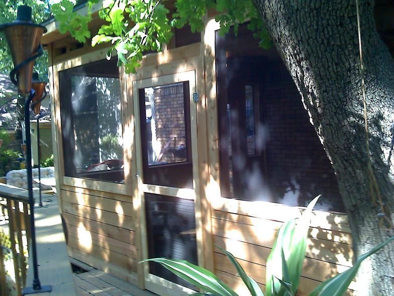 Wooden outdoor structure with screen windows, door, and a tree trunk growing through it.
