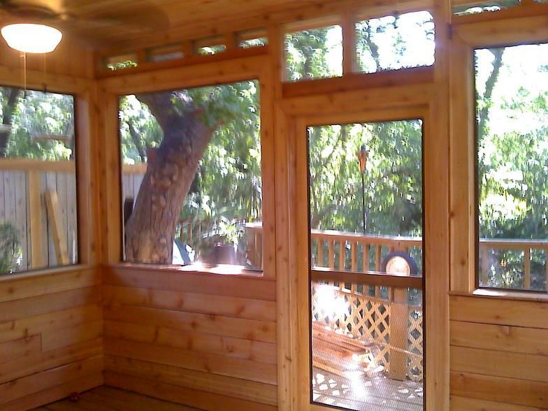Wooden screened porch with windows and a door overlooking a tree and deck.