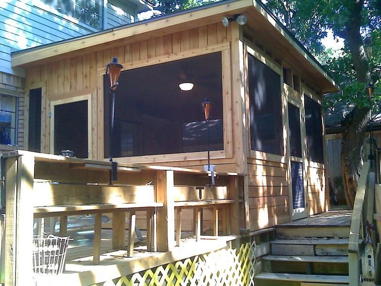 Wooden screened-in porch with deck and steps. Brown siding, black screens, and outdoor lights.