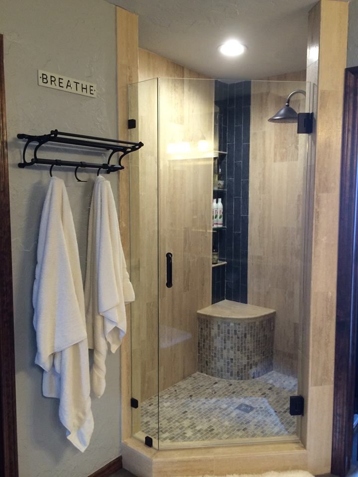 A shower with wood-look tile, glass door, a wooden stump seat, and white towels hanging nearby.