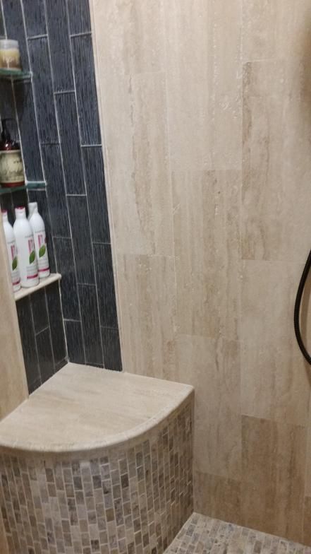 Shower interior with tan and dark blue tile, a built-in bench, and a shelf with toiletries.