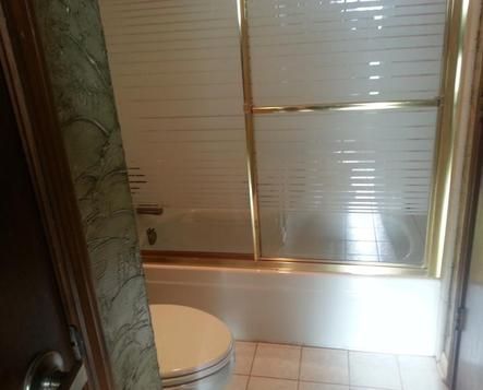 Bathroom with toilet, bathtub, and glass shower door; gold trim.