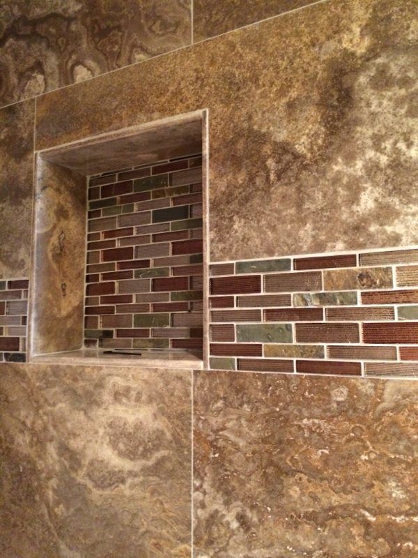 Shower with recessed shelf, featuring brown and multicolored tile accents.