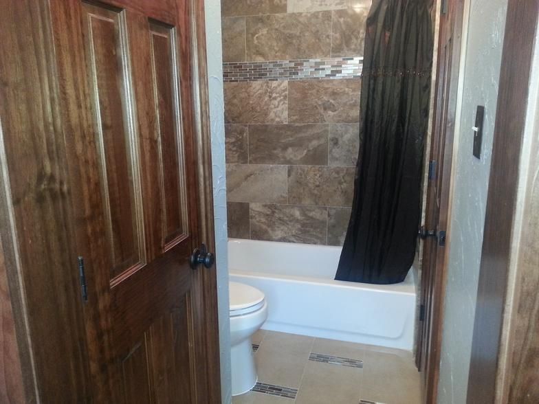 Bathroom interior with wooden door, tiled shower/tub, and toilet.