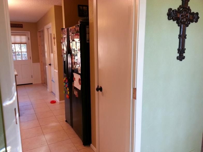 Hallway with tile floor, refrigerator, and door leading to kitchen. A decorative cross hangs on the wall.