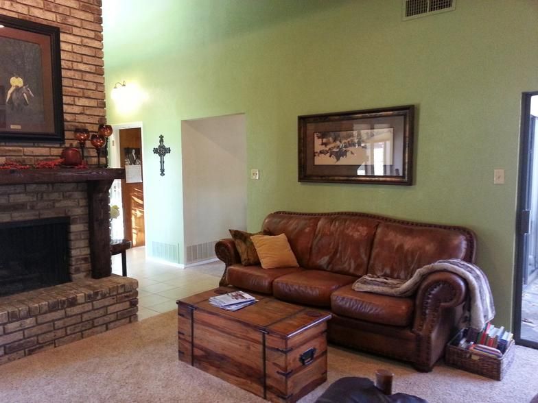 Living room with brown leather sofa, brick fireplace, and trunk coffee table. Green walls and beige carpet.