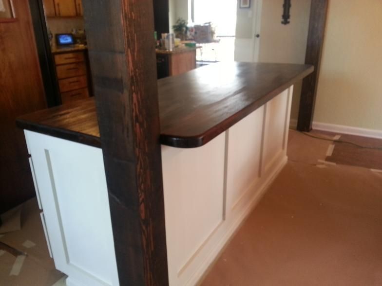 White kitchen island with a dark wood countertop and support beams.