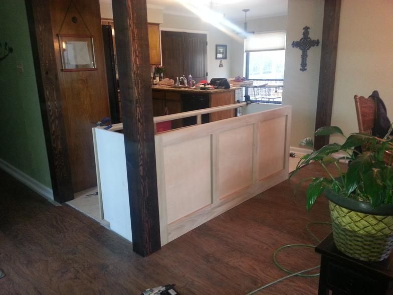 Half-wall under construction, with wooden pillars and cabinets. Kitchen and dining area visible in the background.