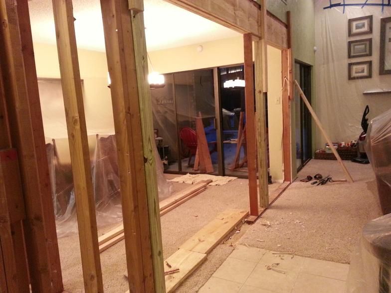 Interior renovation: doorway frame constructed, debris on floor, sliding glass door visible in the background.