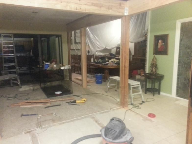 Interior renovation: wooden beams, partially demolished floor, tools scattered about, sheet covering furniture.