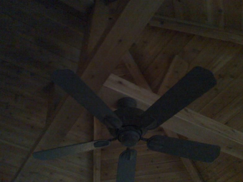 Ceiling fan with four dark gray blades, mounted on a wooden ceiling with exposed beams.