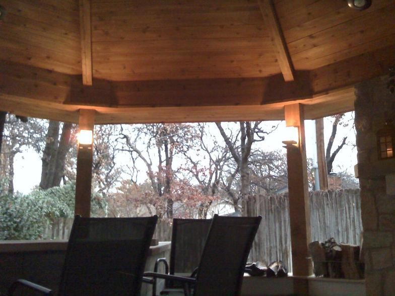 Wooden gazebo interior with chairs overlooking bare trees. Warm lighting.