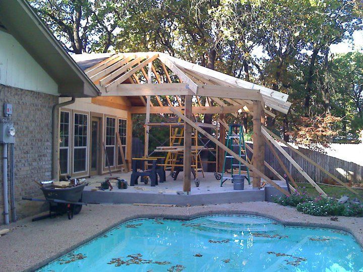 Patio roof construction over concrete patio near swimming pool, partially framed with lumber.