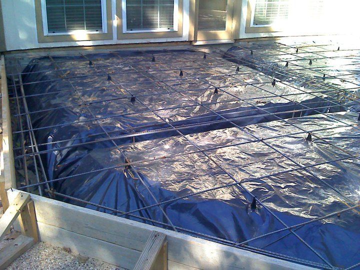Construction site: Rebar grid over a black plastic sheet, ready for concrete pouring on an outdoor patio.