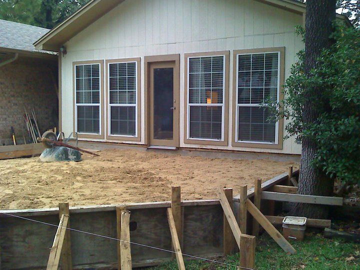 Backyard with construction: windows, door, sand, retaining wall, and tree.