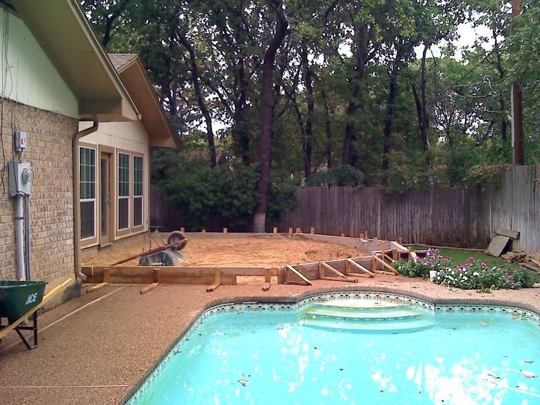Backyard with a pool, concrete patio, and wooden forms in progress for a deck.