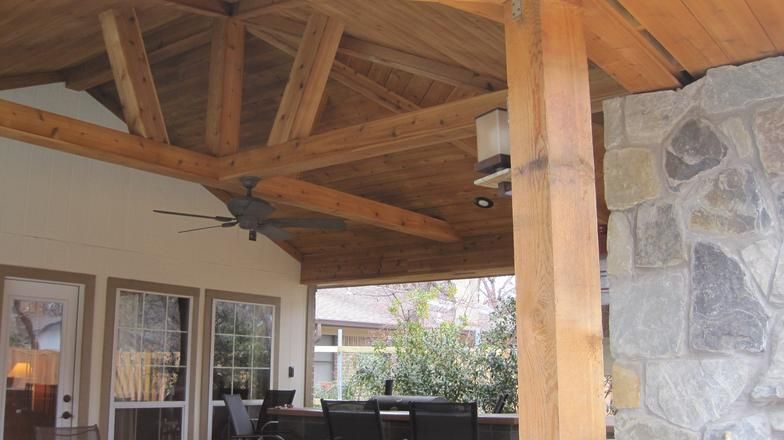 Covered patio with wooden beams, stone wall, and ceiling fan.
