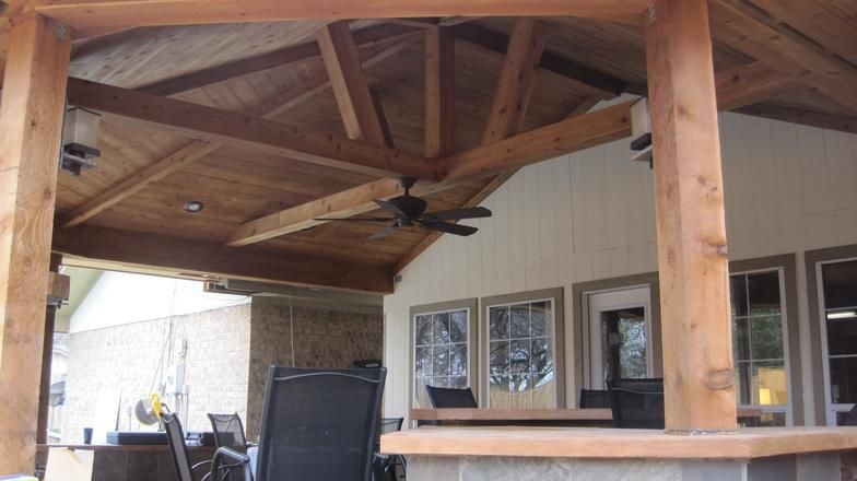 Wooden covered outdoor patio with ceiling fan, seating, and windows.