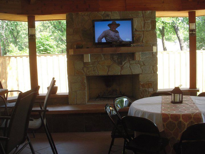 Gazebo interior with stone fireplace, TV, round table with centerpiece, chairs, and surrounding windows.