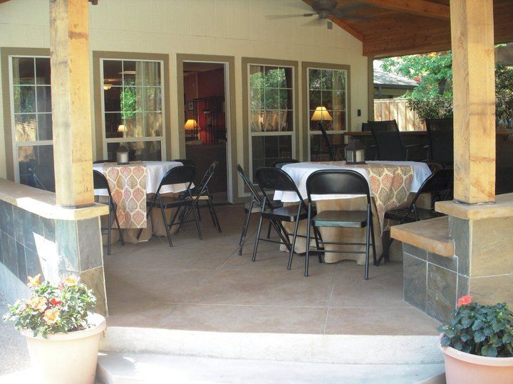 Covered patio with tables set for guests, potted plants.