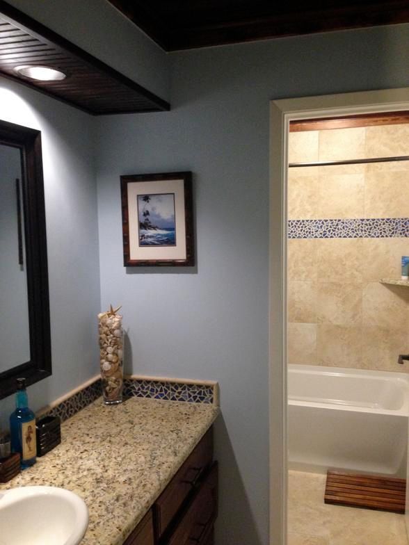 Bathroom with light blue walls, dark wood trim, granite countertop, and framed art.