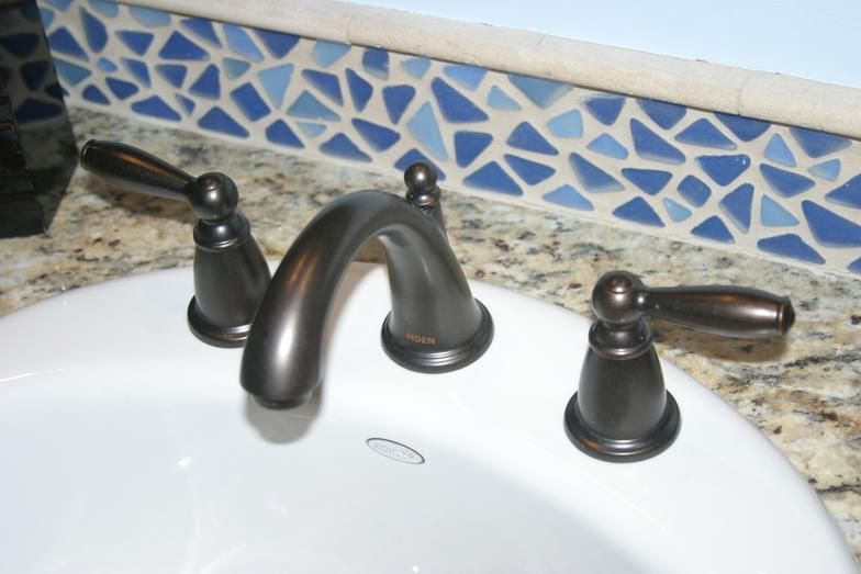Bronze faucet on a white sink, with blue mosaic tile backsplash and granite countertop.