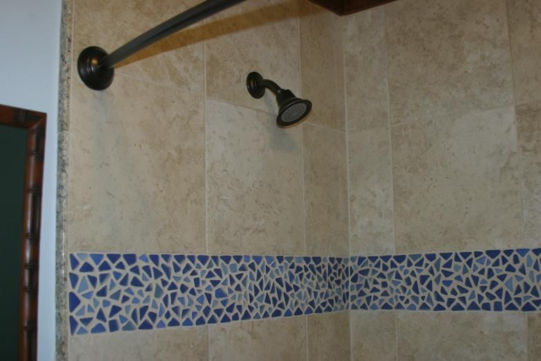 Shower with tan tile walls, blue mosaic border, and bronze fixtures.