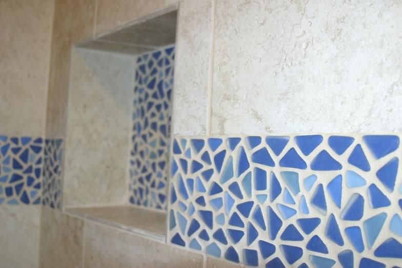 Bathroom shower wall with a mosaic tile border and recessed shelf.