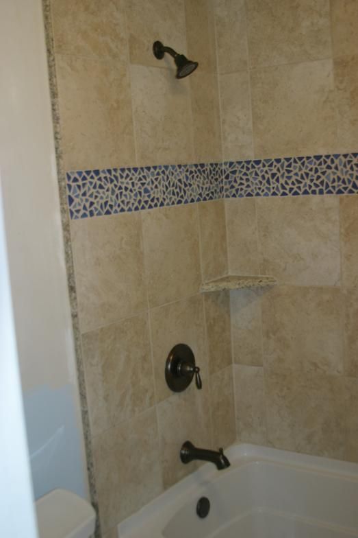 Bathroom with beige tile walls, blue mosaic accent, and bronze fixtures over a white bathtub.