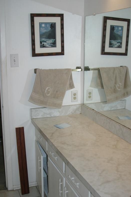 Bathroom with a beige countertop, mirror, framed artwork, and a towel rack with a beige towel.