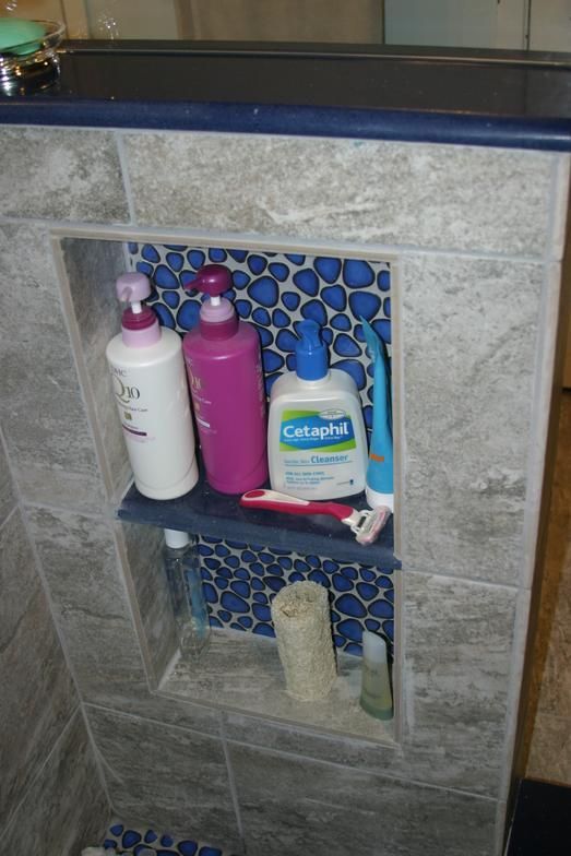 Shower niche with blue mosaic tile backing, holding toiletries like shampoo and cleanser.