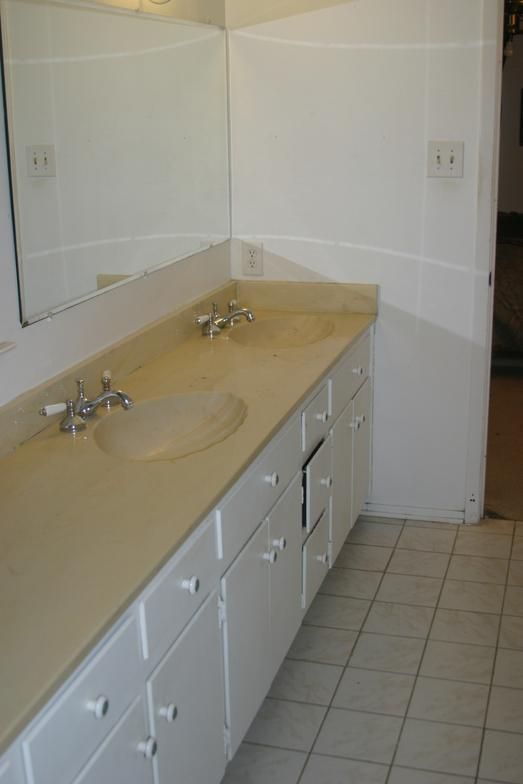 Bathroom with double sinks, white cabinets, beige countertop, and tiled floor.